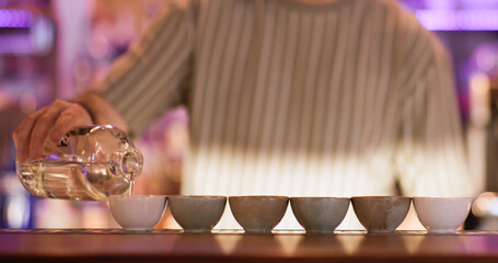 Oriental liquor. Bartender occupation. Man pouring rice wine sake from bottle to clay bowls. Barkeeper filling cups with asian alcoholic liquid.