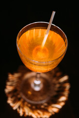 Exotic beverage. Sweet cocktail. Yellow liquid served with orange lollipop in wineglass. Caramel aroma flavor drink isolated on black.