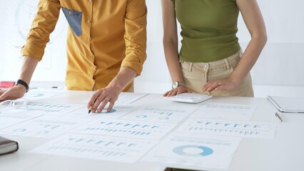 Business colleagues are working together, analyzing financial data and reports using a keyboard and printed charts spread out on a table in a modern office environment
