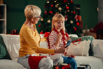 Grandmother and granddaughter making a christmas video call on smartphone