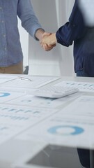 Business partners shaking hands after successful agreement over financial documents, calculator and pen on white table in office. Handshake concept
