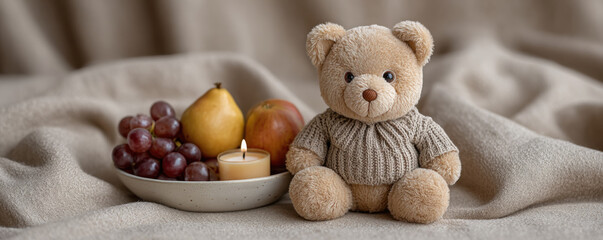 Cozy teddy bear in sweater sits beside plate of fruits and lit candle, creating warm and inviting scene
