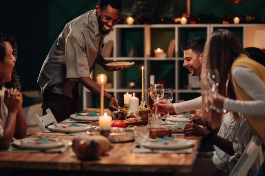 Happy friends enjoying festive dinner, host serving food at candlelit table
