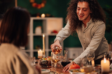 Young man pouring white wine for friends at thanksgiving dinner