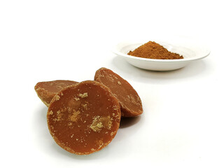 three pieces of natural brown palm sugar or javanese sugar in semicircular shapes and in powder form in white plate isolated on white background