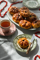 Pumpkin shaped yeast buns with marzipan filling served on vintage plates with tea and natural Autumn decorations on the table.