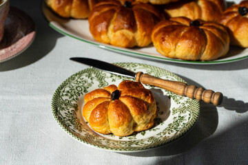 Pumpkin shaped yeast buns with marzipan filling served on vintage plates with tea and natural Autumn decorations on the table.