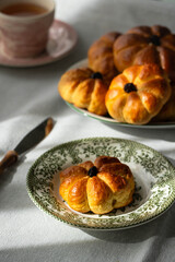 Pumpkin shaped yeast buns with marzipan filling served on vintage plates with tea and natural Autumn decorations on the table.