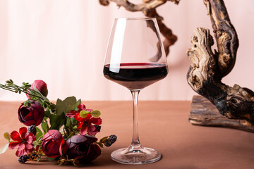 A glass of red wine with a composition of old wood and flowers. Minimalistic composition with light background for wine product branding