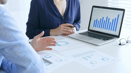 Business professionals collaborating on a laptop, reviewing financial documents, and discussing project strategies in a modern office. Businesspeople in finance concept