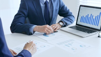 Business colleagues discussing financial data on a laptop and printed documents while analyzing charts and market trends. Business people and finance concept