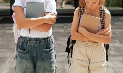 Rear view of multiethnic elementary middle school girls gen Alpha pupils classmates with backpack in casual clothes are hugging embracing each other standing outdoors. Part of a series