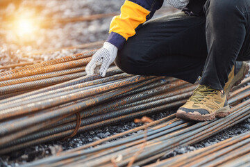 Worker in Safety Gear Examining Steel Rebars on Construction Site During Bright Sunset, Close-Up of...