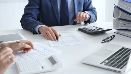 Close up of male financial analysts with female colleague examining documents, using magnifying glass and calculator at workplace in office. Audit and taxes in business