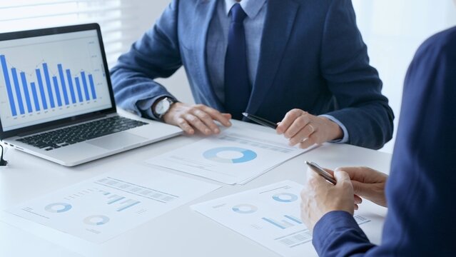 Businesspeople colleagues are reviewing financial data, analyzing charts and graphs, pointing at laptop screen during corporate meeting. Business people and finance concept