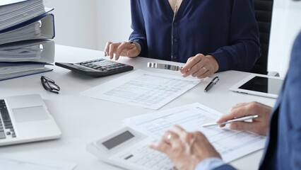 Business team of male and female accountants analyzing financial documents, using calculators and laptop, working together on project in modern office. Audit and taxes concept