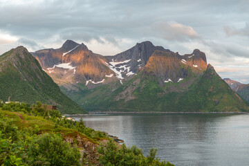 View during midnight sun from Husøy toward wonderful mountains on Senja island, Norway. Hiking destination during cloudy summer day on Senja island. Arctic island in Norway. Some snow on mountains.