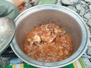 Rustic outdoor meat stew in iron pot – traditional campfire cooking scene