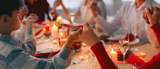 Big extended family praying before festive dinner, holding hands, giving thanks to God at home, selective focus. Celebrating Thanksgiving or Christmas with nears concept