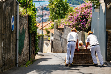 Men push wicker toboggan with passenger down Madeira street.