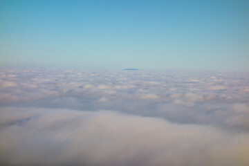 A minimalist and serene view from a high elevation shows a vast marine layer of clouds stretching to the horizon with the distant Palos Verdes peninsula barely visible in the center.
