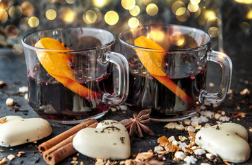 orange slice in mulled wine in two glasses with heart-shaped cookies  and spices  arranged on blur lights  background