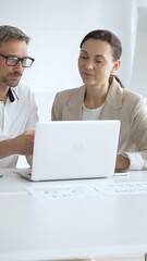 Fototapeta premium Businessman and adult businesswoman reviewing marketing analytics on laptops, working together strategically in contemporary workplace with minimalist interior design and collaborative atmosphere