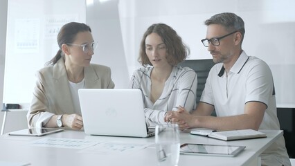 Professional team reviewing project data on laptop, working together in modern office environment, collaborating with focused corporate energy. Business people concept
