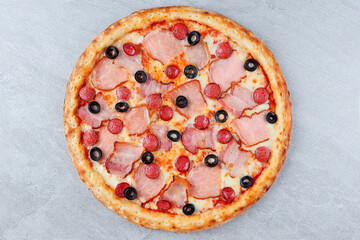 Pizza with Ham, Mini Pepperoni Slices, Black Olives, and Melted Cheese on Crispy Crust over Gray Stone Background