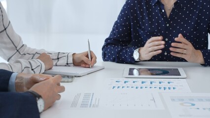 Business people examining and discussing financial documents, studying performance charts on paper and digital tablet during collaborative meeting in modern office