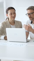 Businessman and adult businesswoman reviewing marketing analytics on laptops, working together strategically in contemporary workplace with minimalist interior design and collaborative atmosphere