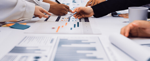 A diverse team of professionals engages in a collaborative meeting, analyzing financial reports and data charts in a modern office space, fostering innovative solutions. SACTR