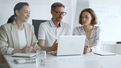 Obraz premium Business people team collaborating on a project, analyzing data on a laptop during a productive office meeting, demonstrating teamwork and problem solving skills