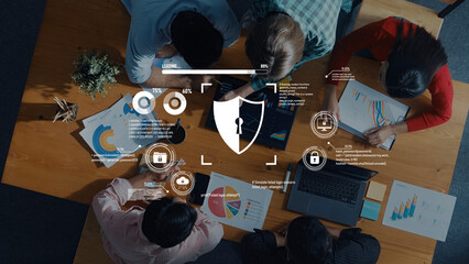 A diverse group of professionals collaborating at a modern office table, analyzing data security and analytics visualizations while engaging with technology and charts. Trope