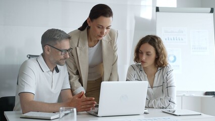 Fototapeta premium Business people team collaborating on a project, analyzing data on a laptop during a productive office meeting, demonstrating teamwork and problem solving skills