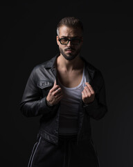 Naklejka premium cool fashion man with sunglasses pulling and adjusting black leather jacket
