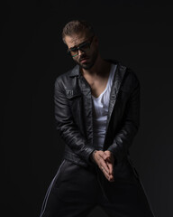 Obraz premium dramatic fashion man with sunglasses in black leather jacket rubbing palms