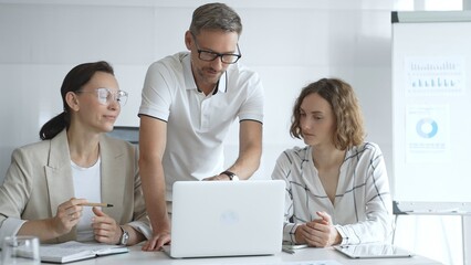 Professional team working together, reviewing data on laptop screen, sharing insights in contemporary workspace, highlighting collaborative corporate environment