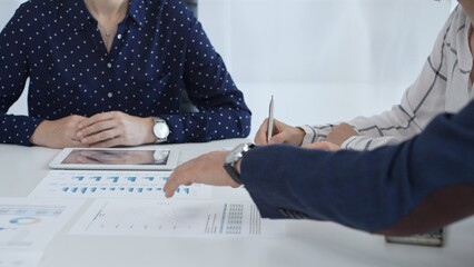 Business people examining and discussing financial documents, studying performance charts on paper and digital tablet during collaborative meeting in modern office