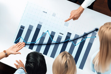 A business team works together analyzing a financial growth graph. The collaborative atmosphere fosters communication and strategic planning in a modern office setting. Axiom