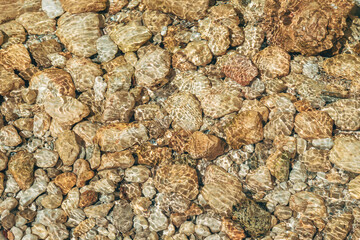 Rocks at the bottom of a mountain creek with sunlight caustic effect on clear water surface.