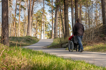 Person in wheelchair and a helper having relaxing walk on curvy park path. A man walks with a woman in wheelchair at forest. Friend is assisting person in wheelchair during hike. 