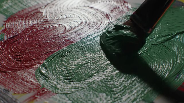 Close-up of a paintbrush applying green and red paint on canvas, artistic texture background, painting, art.