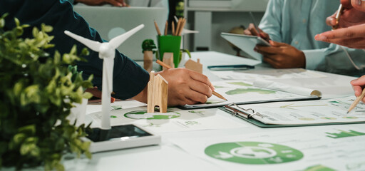 A modern office scene showcasing hands engaged in a sustainable project with a wind turbine model, eco-friendly documents, and collaborative efforts on green initiatives. SACTR