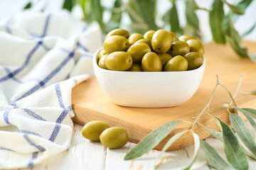 Green olives in bowl with fresh olive leaves. Greens olives on a white wooden table.