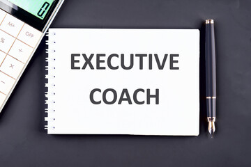 Business concept. The phrase, the text, the word EXECUTIVE COACH are written in a notebook on a dark blue background
