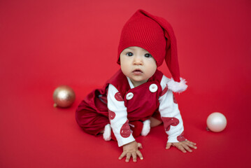 A little girl in a smart red suit, dressed as a gnome, sits on a red background for the New Year's holiday.