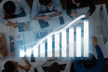 A diverse group of business professionals collaborates on financial analysis with graphs overlaying their discussion, showcasing trends and strategies in a modern office. Axiom