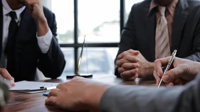 Experienced business professionals negotiating contract details, analyzing documents with focused body language and strategic hand gestures while seated at wooden conference table