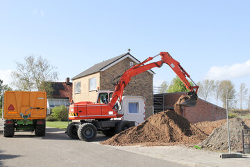 a construction site with heaps of ground and an excavator and a tipping trailer in the countryside